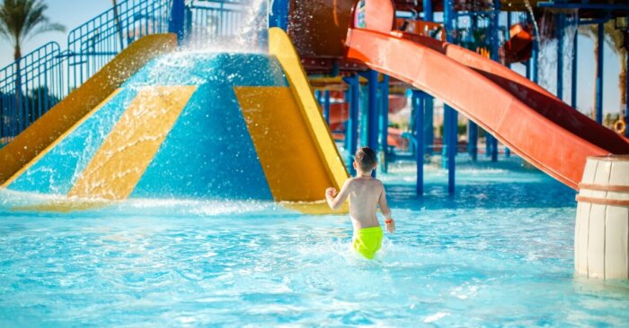 A boy wearing bright yellow swim trunks walks inside a shallow pool in a colorful play area at a water park. A boy wearing bright yellow swim trunks walks inside a shallow pool in a colorful play area at a water park.