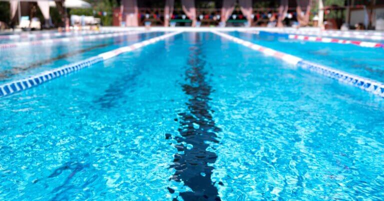 Close-up of a lane in a large swimming pool with clear water, with multiple floating ropes and cabanas in background.
