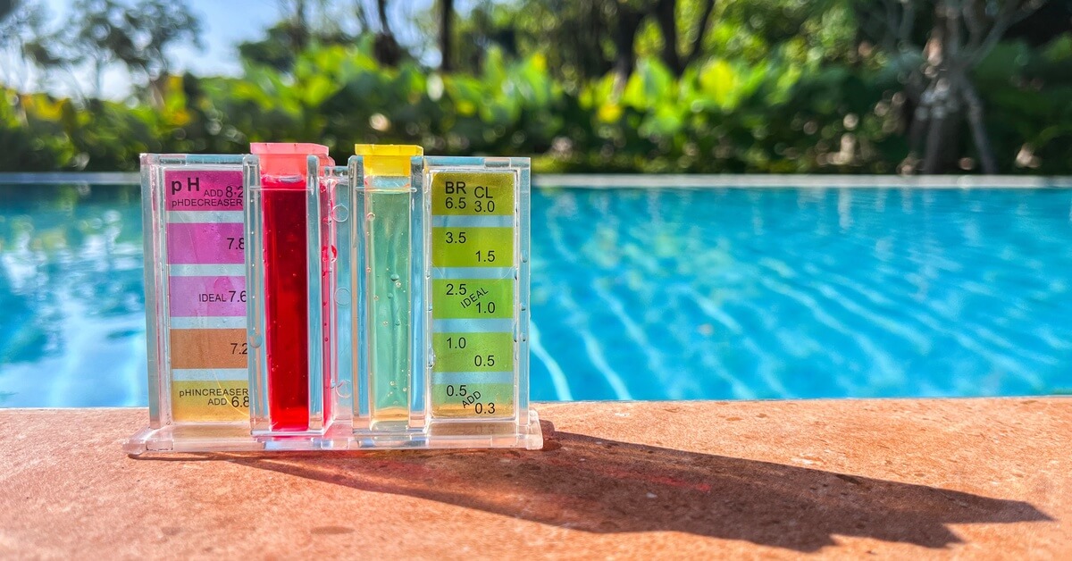 A water sample testing kit with different color blocks and two tubes full of water is on the ground next to a pool.