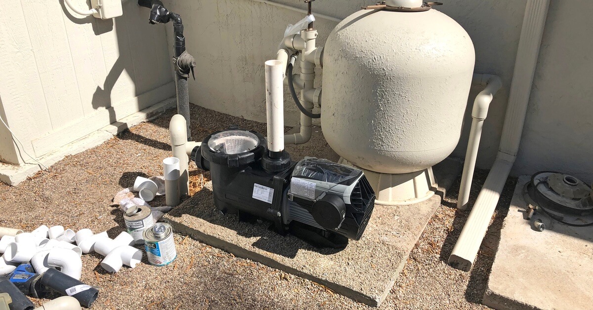 New black swimming pool pump on the ground next to a large distributor with multiple PCV pipes and connectors.