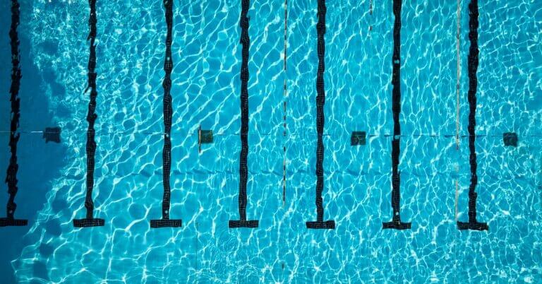 An aerial view of a large pool with clear water, straight black underwater lane lines, and small hanging flags.