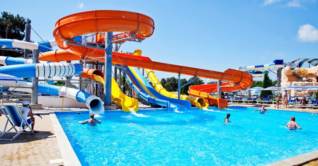 A large water park with multiple water slides in different shapes and colors, leading to a large pool with people in it.