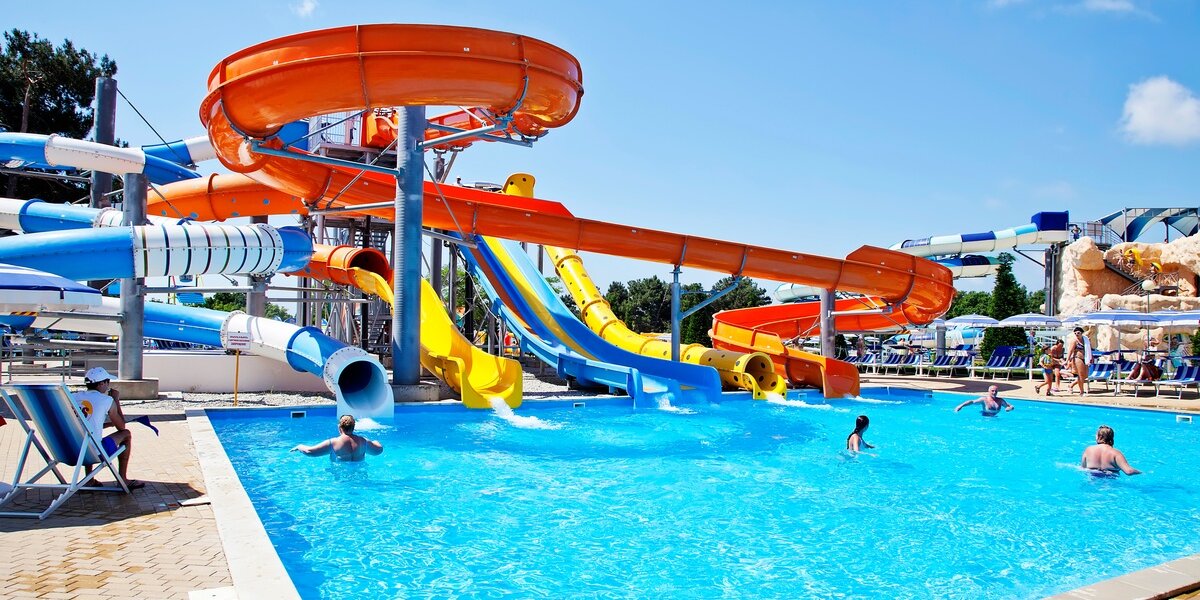 A large water park with multiple water slides in different shapes and colors, leading to a large pool with people in it.
