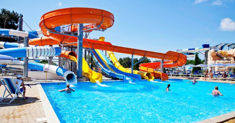 A large water park with multiple water slides in different shapes and colors, leading to a large pool with people in it.